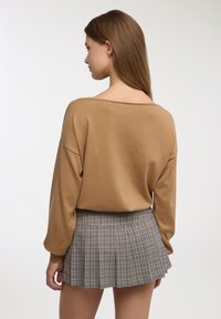 Maglione marrone dalla vestibilità ampia con spalle scese abbinato a una minigonna plissettata a quadri nei toni del beige e del blu navy. Tessuto dalla trama liscia.