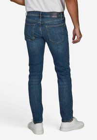 Schmale blaue Denim-Jeans mit fünf Taschen, Kontrastnähten und Lederpatch am Bund. Kombiniert mit weißen Sneakern.