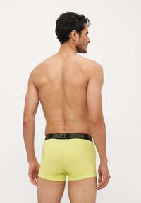 Gule boxershorts laget av myk bomullsblanding, med et svart elastisk liv med merkets logo tydelig vist.