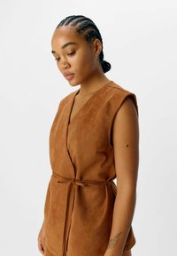 Robe sans manches en suède marron avec un décolleté en V et une taille à lien à nouer. Présente une texture lisse et une silhouette décontractée.