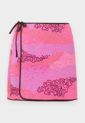 Jupe portefeuille matelassée rose avec motifs abstraits brodés multicolores et bordure brun foncé nouée à la taille.