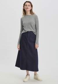 Grauer Langarmpullover kombiniert mit einem knöchellangen, dunkelblauen Jeansrock. Das Outfit wird mit hellfarbigen Turnschuhen abgerundet.