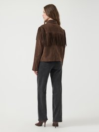 Veste en daim marron avec des franges sur les épaules, associée à un jeans noir à jambe droite et des chaussures à talons hauts marron.
