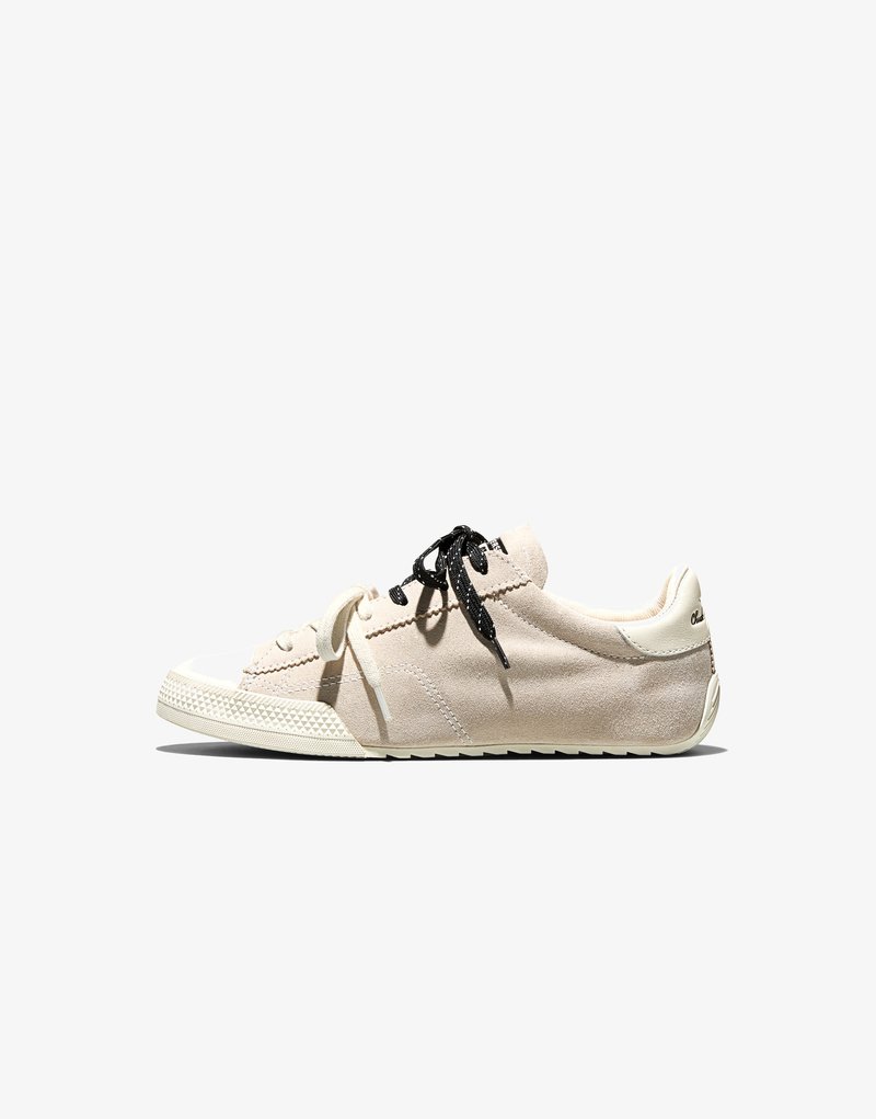 Beżowy zamszowy sneaker z rozdzielonym noskiem, czarno-białe sznurówki oraz teksturowana gumowa podeszwa, widoczny z boku na białym tle.