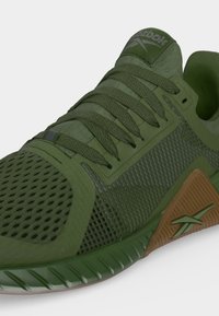 Πράσινο αθλητικό παπούτσι Reebok με υφαντό διχτυωτό επάνω μέρος, κορδόνια και καφέ πλαϊνή στήριξη με το λογότυπο Reebok.