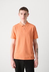 Polo majica kratkih rukava u jarkoj narančastoj boji od pamuka, s klasičnom ovratnikom, tri gumba i suptilnim izvezenim logom na prsima.