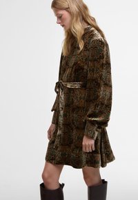 Βελούδινο ρόμπα σε σκούρο πράσινο χρώμα με περίπλοκα καστανά λουλούδια. Διαθέτει ζώνη στη μέση, μακριά μανίκια και φαρδύ φουστάνι. Λείο υλικό.