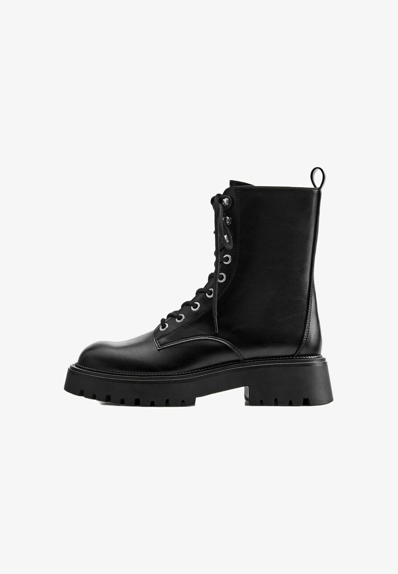 Botte de combat noire en cuir à lacets avec semelle en caoutchouc épaisse et languette à l’arrière, vue de côté sur fond blanc.