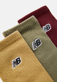 Three pairs of socks in mustard yellow, olive green, and burgundy, featuring ribbed texture and embroidered New Balance logo.
