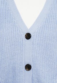 Γαλάζιο πλεκτό ζακέτα με σχέδιο V λαιμόκοψης, υφή υφάσματος και τρία μαύρα πλαστικά κουμπιά μπροστά.