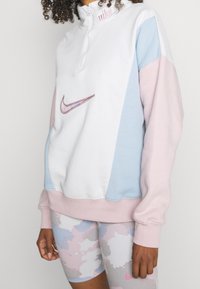 Sweatshirt Nike  à demi-zip, avec un corps blanc et des manches rose et bleu clair. Logo brodé à l'avant, tissu doux, coupe décontractée.