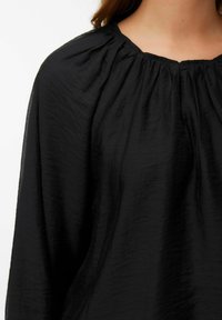 Blusa nera in tessuto leggero e testurizzato. Presenta un colletto arricciato e maniche fluide. Il design semplice enfatizza il comfort.