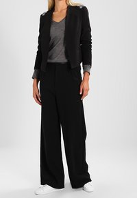 Černý cropped blazer s ozdobami, šedé tričko, černé široké kalhoty a bílé tenisky. Hladká tkanina se strukturovaným designem.