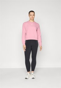 Sweat-shirt rose à col rond et ourlet côtelé, accompagné de leggings noirs avec des bandes blanches sur les côtés et des chaussures de sport grises.