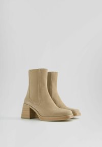 Beige kotníkové boty vyrobené z měkké látky, s čtveratou špičkou, elastickými bočními panely a masivním, texturovaným dřevěným podpatkem.