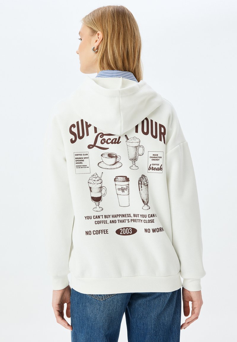 Sudadera blanca con un estampado gráfico en la parte trasera que muestra ilustraciones de café y texto en marrón. Tejido suave con un corte relajado y capucha.