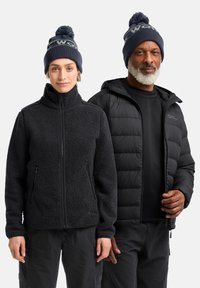 Black fleece jacket with zip and side pockets on the left; black puffer jacket with hood and front zip on the right; both wear knitted hats.
