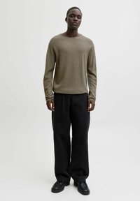 Olivgrön tröja med rund halsringning, kombinerad med svarta vidbyxiga byxor och svarta skor. Tyget har ett mjukt och strukturerat utseende.