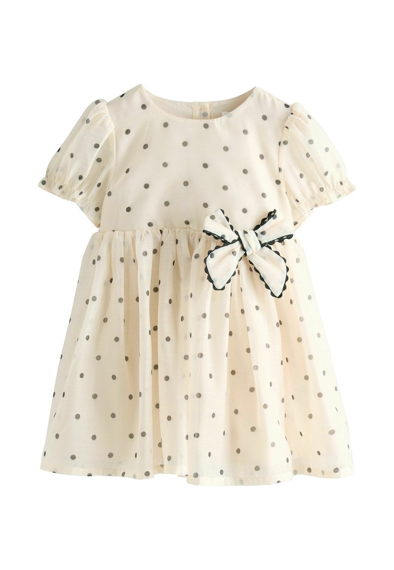 Jasnobeżowa sukienka w szare kropki, z krótkimi bufkami i marszczonym pasem. Z przodu znajduje się detal w postaci kokardy z falbaniastym wykończeniem.