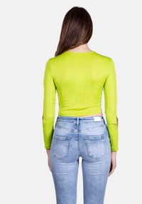 Maglietta verde lime aderente a maniche lunghe con texture a coste, abbinata a jeans in denim blu chiaro con dettagli sulle tasche e una finitura leggermente sbiadita.