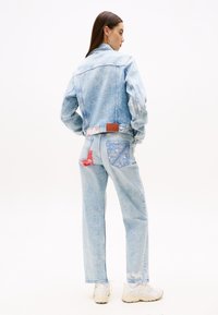 Svetlomodrá džínsová bunda a nohavice s rôznymi odtieňmi a kontrastnými látkovými záplatami, s textúrovaným povrchom a voľným strihom.