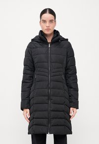 Melnā pūkaina jaka ar rāvējslēdzēju priekšā, kapuci un sānu kabatām. Šuvei saskaņota un quilted tekstūra nodrošina siltumu un stilu.