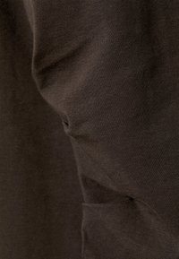 Mørkebrunt stoff med en jevn, svakt teksturert overflate. Materialet viser naturlige folder og varierende lysrefleksjoner.