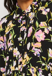 Abito nero floreale con fiori viola, rosa e gialli. Tessuto morbido con colletto, dettagli a bottoni e design plissettato.