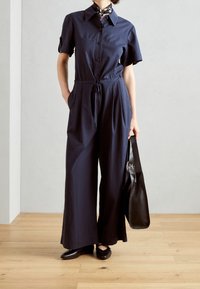 Granatowy kombinezon z krótkimi rękawami, zapięcie na guziki, ściągacz w talii i szerokie nogawki. W zestawie czarna torebka i baleriny.