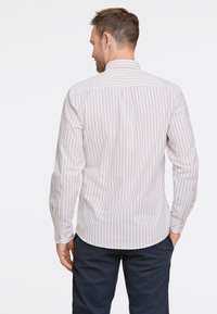 Camisa a rayas suaves en beige y blanco, de mangas largas, con puños abotonados, detalle en el yugo trasero, corte entallado. Se lleva con pantalones azul marino.