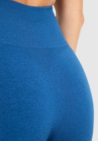 Blå højtaljede leggings lavet af strækbart stof med en glat overflade. Har et sømløst design og et diskret meleret mønster.