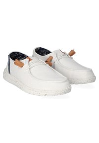 Chaussures blanches en tissu avec une surface texturée, des accents en cuir marron et une doublure intérieure à motifs. Elles comportent une semelle flexible avec des éclats.