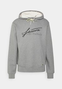 Sudadera gris, mezcla de algodón, con capucha ajustable con cordón, bolsillo canguro, texto de logo en negro y un pequeño emblema de cocodrilo verde.