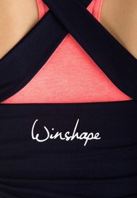 Sötétkék ujjatlan póló keresztpántos háttal, rózsaszín belső póló fölött. A "Winshape" logó fehér színben nyomtatva a sötétkék részre. Puha szövettextúra.