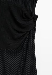 Czarna tkanina z dwoma małymi wzorami w kropki, zebrała się i została zawiązana po prawej stronie na białym tle.