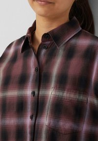 Flanellen shirt in bordeauxrood en zwart geblokt patroon, met een knoopsluiting aan de voorkant, zwarte knopen en een enkele borstzak. Glad textuur.