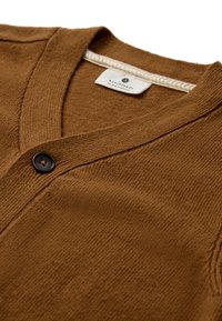 Cardigan marrone lavorato a maglia con scollo a V, chiusura con un singolo bottone nero e tessuto traforato con un motivo sottile. Etichetta visibile all'interno.