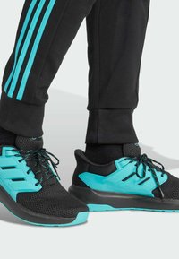 Black athletic shoes feature a mesh upper, turquoise accents, and black laces, paired with black pants with turquoise side stripes.