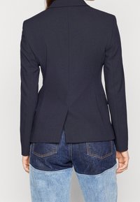 Granatowa, dopasowana marynarka z pojedynczym rozcięciem z tyłu, usztywnionymi ramionami i długimi rękawami, zestawiona z dwukolorowymi jeansami.