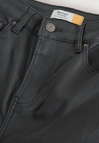 Czarne dżinsy bootcut z średnim stanem, z widocznymi szwami, metalowymi elementami i metką z napisem "BOOTCUT MID RISE."