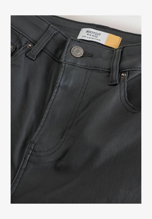 Černé bootcut džíny s středně vysokým pasem, které mají viditelné švy, kovové doplňky a štítek s označením "BOOTCUT MID RISE."