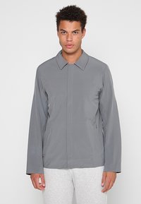 Graue leichte Jacke mit langen Ärmeln, einem Kragen und geradem Schnitt. Verfügt über Seitentaschen und eine glatte, matte Oberfläche.