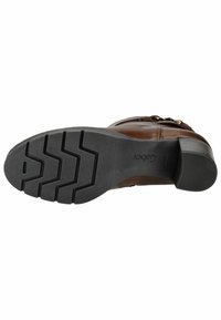 Botte en cuir marron avec une semelle en caoutchouc noir texturé, arborant un motif en zigzag et un petit talon empilé. Accent de boucle sur le côté.