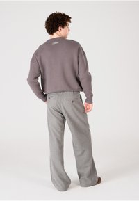 Pull en maille gris avec un col rond et des poignets côtelés, associé à un pantalon large gris clair comportant deux boutons à l'arrière.