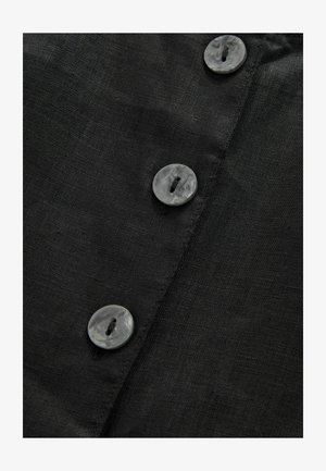 Tessuto di lino nero con quattro bottoni rotondi in grigio marmorizzato. Nota la texture visibile del tessuto e la disposizione dei bottoni lungo la cucitura.