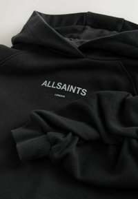 Melns kokvilnas kapučjakas ar auklu kapuci, ribām apakšdelma aprocēs un baltu "ALLSAINTS LONDON" logotipu priekšpusē. Mīksta tekstūra.