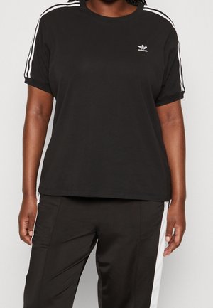 Osoba nosząca czarną koszulkę Adidas z białymi paskami na rękawach oraz dopasowane czarne spodnie z białymi paskami po bokach.