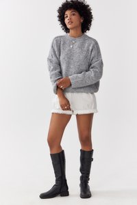 Sivi pleteni pulover s rebrastom teksturom, oversize kroja, uparen s krem kratkim hlačama s čipkastim rubom i crnim kožnim čizmama do koljena.