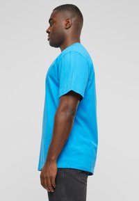 Blue cotton T-shirt with short sleeves, regular fit, featuring a round neckline and a smooth texture, displayed from a side view.