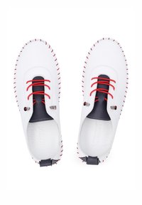 Weiße Lederschuhe mit roten Schnürsenkeln und Nähten, navyblauen Akzenten, runder Form und offenem Design. Auffällige Details sind metallische Elemente.